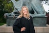 Clarissa in graduation gown poses in front of large Gryphon statue