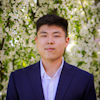 headshot of Peter Kim behind tree blooming with white flowers.