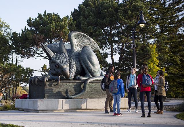 A group of students visits next to the Gryphon statue on the University campus.