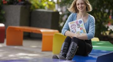 Student with blonde hair sits on one of the rainbow benches on campus.