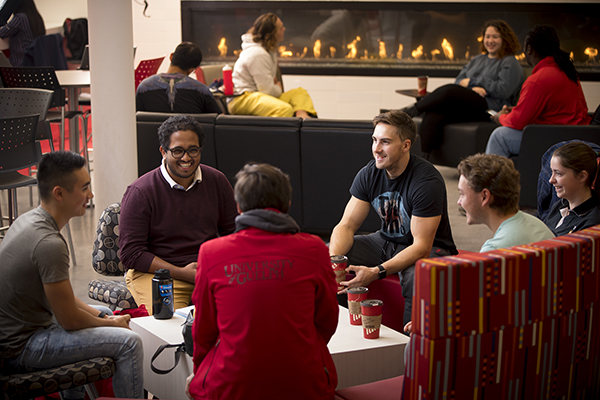 Six students chatting in a campus fireplace lounge