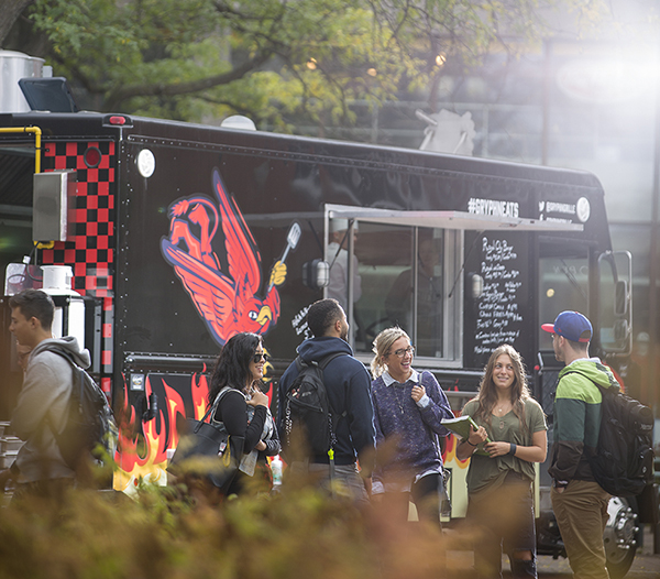 A group of students laughing in front of the Gryphon Grille food truck on campus.